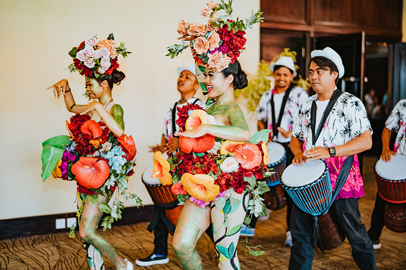 Women dressed in floral arrangements and men with hand drums